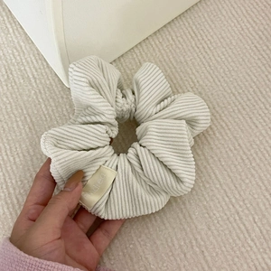 Close-up of cream corduroy scrunchie texture with high-quality brand label detail