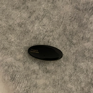 Pince à cheveux ovale en acétate noir avec logo doré sur fond texturé doux