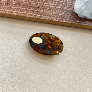 Detail of French tortoiseshell acetate oval hair clip with gold metal logo inlay