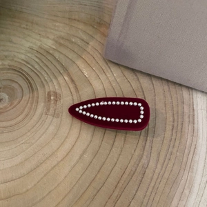 Elegant deep red velvet hair clip with faux pearl border on a natural wooden plate