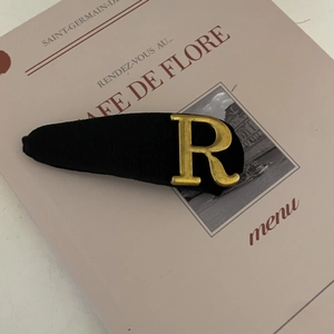 Close-up of black ribbed fabric hair clip featuring a vintage gold metal letter R detail