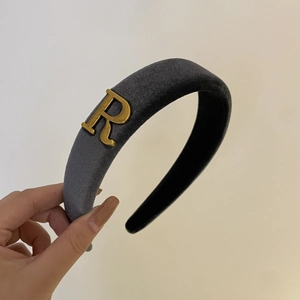 Detail view of the gray velvet headband featuring a golden metallic letter R ornament