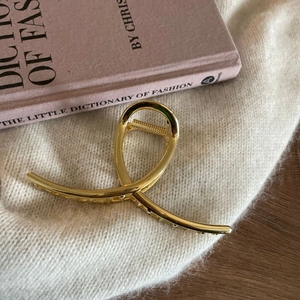 Minimalist gold metal hair claw clip with crossed lines design on white knit fabric