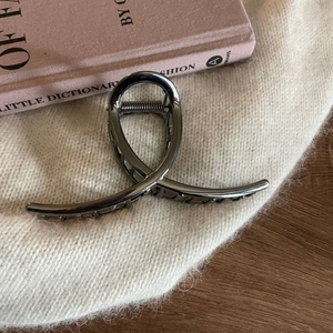 Detail of gun-metal grey twisted metal shark hair claw clip on white knit fabric