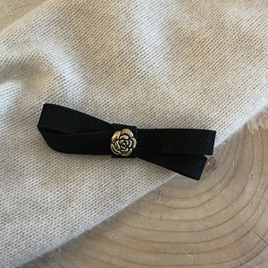 Retro black velvet bow hair clip with a golden camellia flower accent on a soft sweater