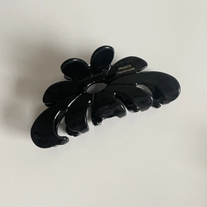 Dettaglio della pinza per capelli a fiore nero fatta a mano con scritta logo dorata