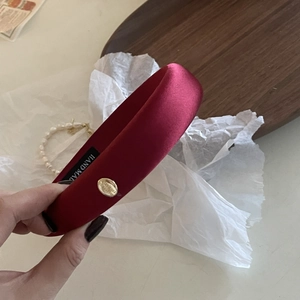 Dettaglio di un cerchietto in raso bordeaux con placca in metallo dorato ed etichetta a mano