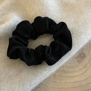 Close-up of black faux leather scrunchie with textured finish on a cozy knit background