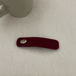 Close-up of a vintage dark red velvet hair clip with a silver engraved metal plate detail