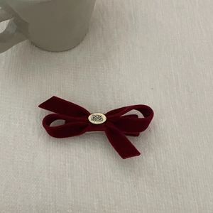 Detailed view of the dark red velvet bow hair clip with gold metal emblem on white fabric