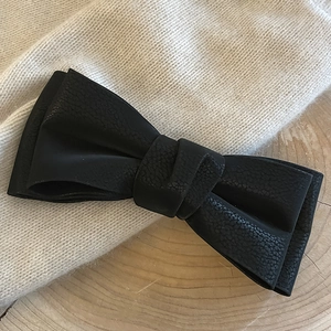 Detail of lychee textured faux leather black bow hairpin on a soft knitted background