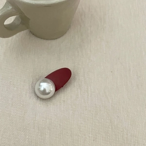 Close-up of elegant red hair clip with large pearl detail on a textured fabric