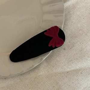 Barrette à cheveux avec nœud en velours rouge sur assiette décorative et fond en lin vintage