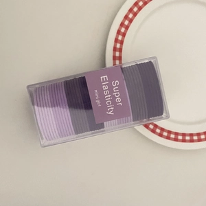 Detail view of purple candy-colored elastic hair ties set in a transparent mini girl box