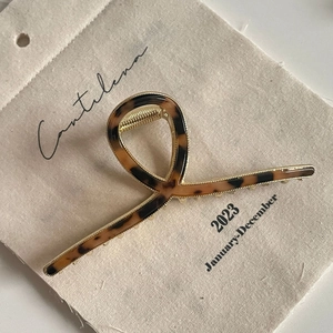 Detail of tortoiseshell acetate hair claw with golden metal trim on beige fabric