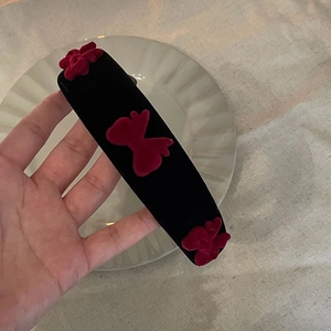 Serre-tête élégant en velours noir avec trois nœuds rouges tenu sur une assiette
