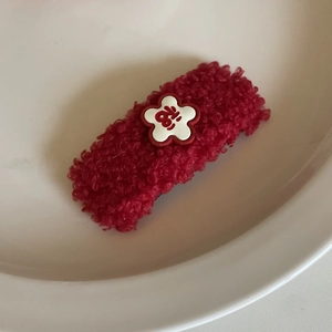 Close-up of red plush hair clip with white flower and Fu character on white ceramic plate