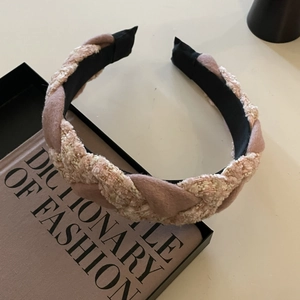Detail view of woven pink tweed headband next to fashion book and black gift box