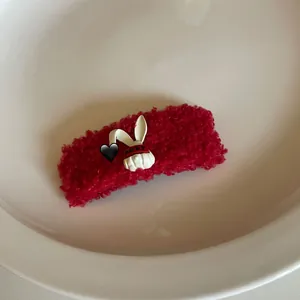 Detail of red plush hair clip featuring a 3D white rabbit with baby lettering embroidery