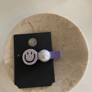 Detail view of purple rhinestone hairpin with a smiley face and pearl ornament decoration