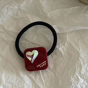 Macro detail of red square charm hair tie with heart crystal and handmade gold lettering