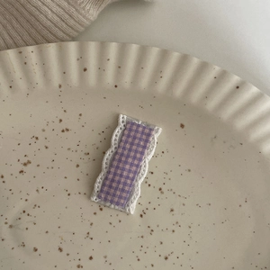 Dettaglio molletta per capelli a quadretti viola con pizzo bianco su piatto di ceramica