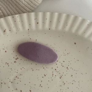 Dettaglio molletta ovale in velluto viola su un piatto in ceramica beige vintage