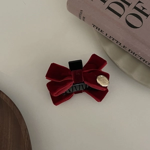 Vintage red velvet bow hair clip with gold metal tag on a fashion book background