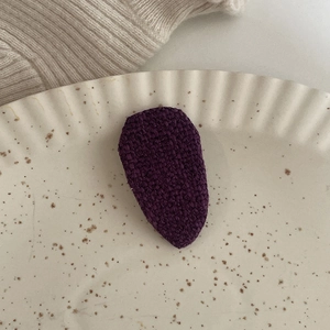 Dettaglio di un fermaglio per capelli a goccia in tessuto viola scuro su un piatto