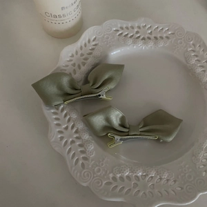Detail view of two avocado green satin bow hair clips in a white lace porcelain plate