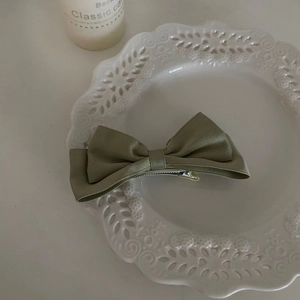 Detail of sage green satin bow hair clip with silver metal alligator clamp on white plate