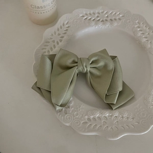 Close-up of elegant sage green satin bow hair clip placed on white ceramic plate