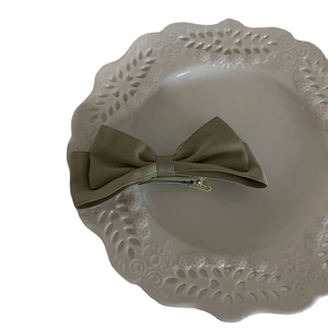 French style dark green satin bow hair clip on a decorative white ceramic plate
