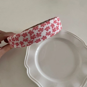 Close-up of white fabric headband with red floral print against a minimalist background