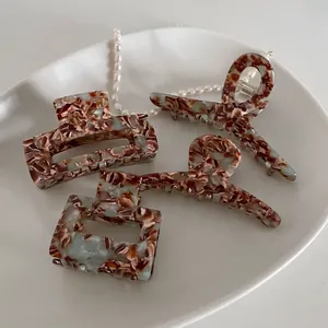 Set of four tortoiseshell acetate hair claws in brown and blue marble textures on a plate