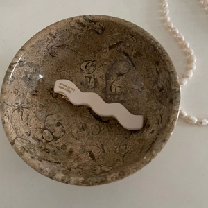 French wavy acetate hair clip in beige with gold lettering in a stone bowl
