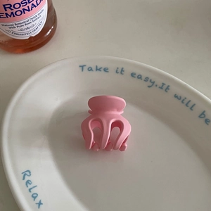 Close-up of a matte pink octopus hair claw clip placed on a white ceramic plate