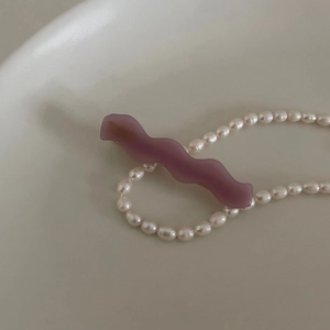 Close-up of a purple wave-shaped acetate hair clip next to a white pearl necklace