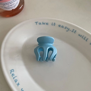 Close-up of a matte light blue hair claw clip placed on a stylish white ceramic plate