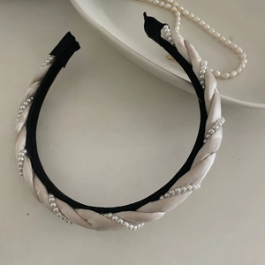 Détail d'un élégant serre-tête tressé en satin champagne et perles sur fond blanc