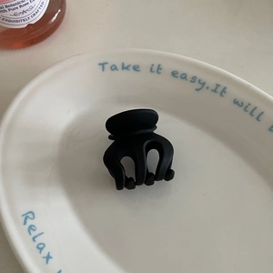 Matte black claw clip in a white ceramic dish, showcasing matte finish and interlocking teeth