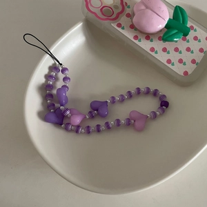 Vue détaillée des perles de cœur violettes et rayées sur une dragonne de téléphone chic
