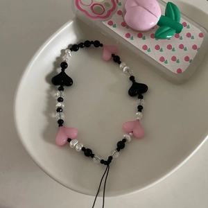 Détail de perles en cœur roses et noires avec perles blanches sur une dragonne de téléphone