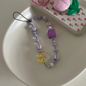 Détail de la dragonne de téléphone perlée avec cubes violets et papillon jaune sur plateau