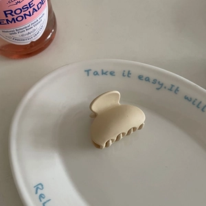 Detail view of a matte cream mini hair claw clip placed on a decorative white ceramic plate