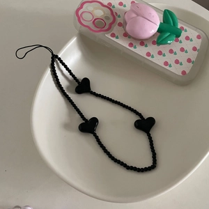 Détail d'une dragonne de téléphone en perles noires avec breloques cœur dans un bol blanc