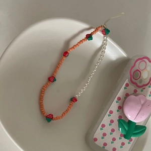 Détail de la dragonne de téléphone avec breloques fraises 3D et perles mates roses