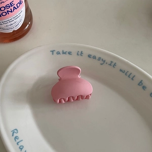 Pink matte claw clip with wavy teeth displayed on a decorative ceramic plate