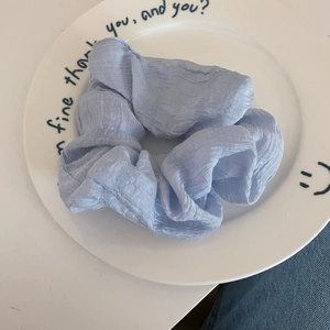 Detailed texture of light blue pleated scrunchie on a white ceramic display plate