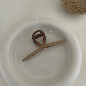 Détail d'une grande pince à cheveux marron mat avec dents antidérapantes sur bol blanc